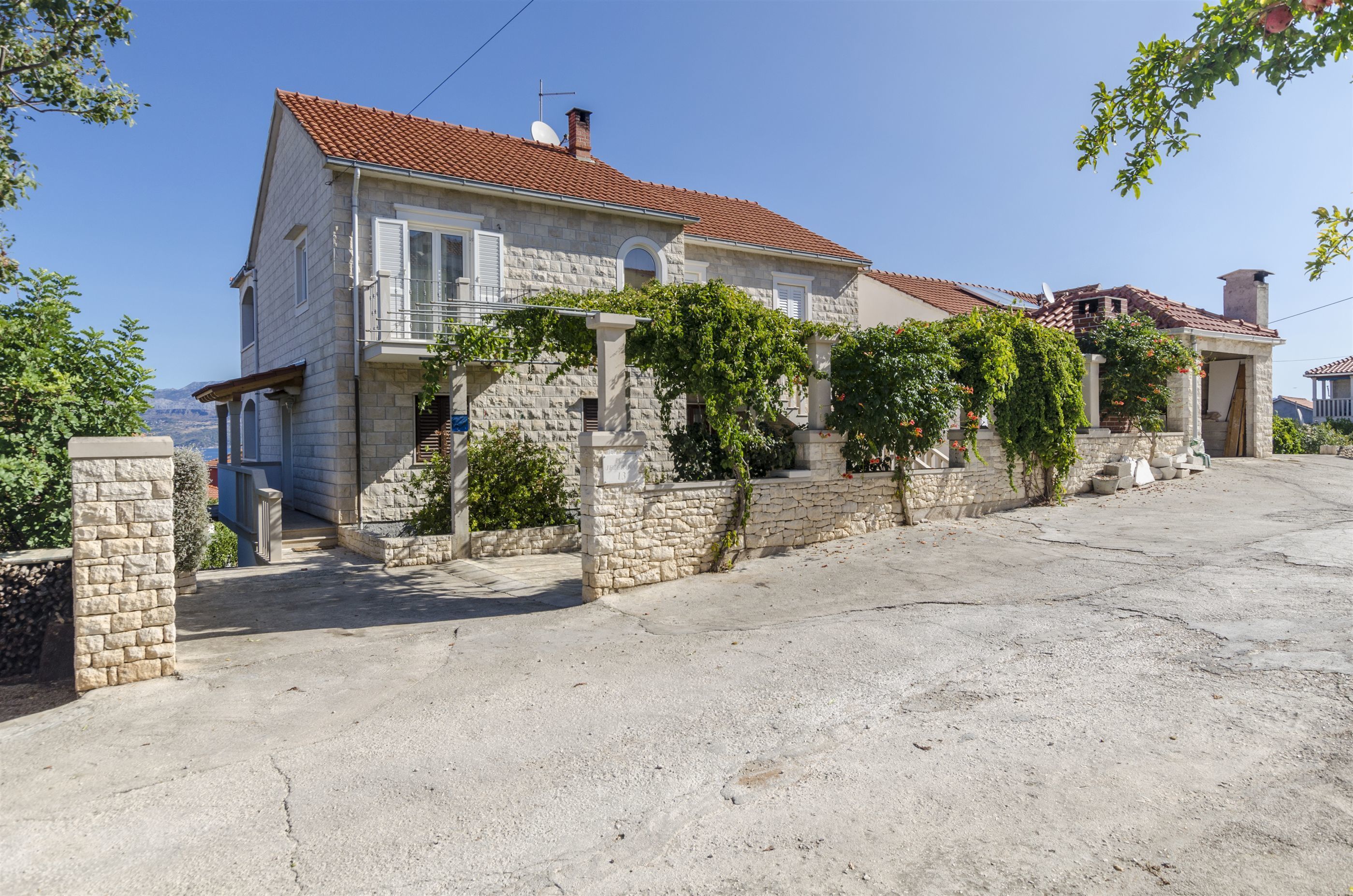 A stone house with a red-tiled roof, a stone staircase, and a garden with climbing plants.