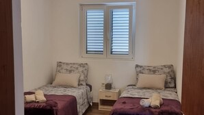 A bedroom with two beds, a window, a nightstand, and a wooden floor. - Apartment Milan (Vrboska)