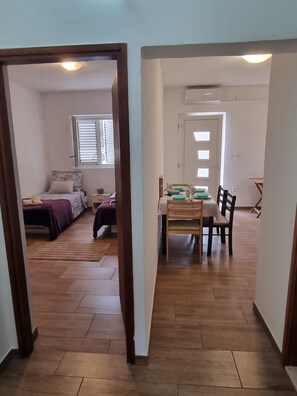 A hallway leading to a bedroom with a bed and a window, and a dining area with a table and chairs. - Apartment Milan (Vrboska)