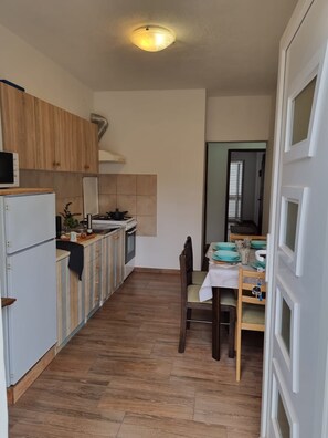 Une cuisine compacte comprenant un coin repas, des meubles de rangement en bois, une cuisinière et un réfrigérateur.