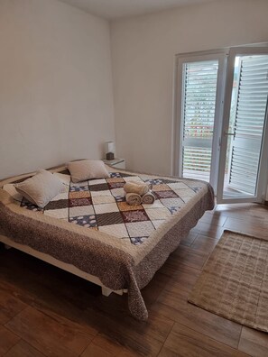 Une chambre à coucher avec un lit, des oreillers, une table de chevet, une fenêtre avec des stores et un plancher en bois.