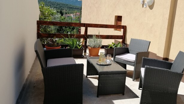 An outdoor patio with wicker furniture, a glass table, and potted plants. - Apartment Milan (Vrboska)
