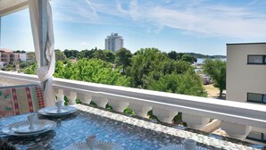 A balcony with a tiled table, a white railing, and a view of a building and trees. - Apartments Plava Plaza Daniela (Vodice)
