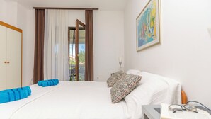 A hotel room with a bed, a window with curtains, a painting on the wall, and a bedside table with a book and glasses. - Apartments Plava Plaza Daniela (Vodice)