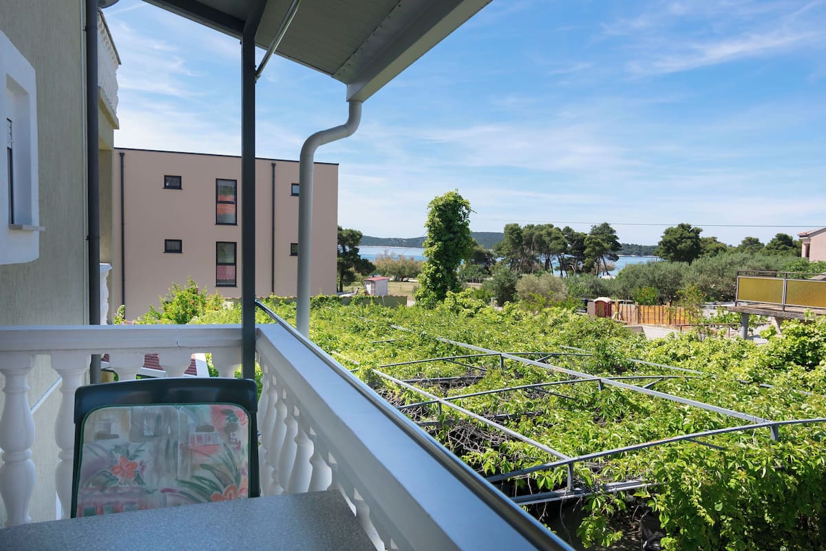 Un balcón con vista a un edificio, vegetación y una masa de agua.