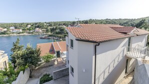 A coastal building with a tiled roof, a balcony, and a view of the sea and surrounding houses. - Apartment Ivo (Basina)