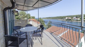 A balcony with a table and chairs, overlooking a body of water and a distant shoreline. - Apartment Ivo (Basina)