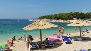 A beach with umbrellas, lounge chairs, and people sunbathing. - Apartment Luketa (Primosten)