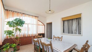 A dining area with a table and chairs, a potted plant, and a window with curtains. - Apartment Luketa (Primosten)