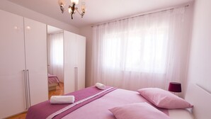 A bedroom with a bed, a mirror, a window with sheer curtains, and a bedside lamp. - Apartments Kure (Primosten)