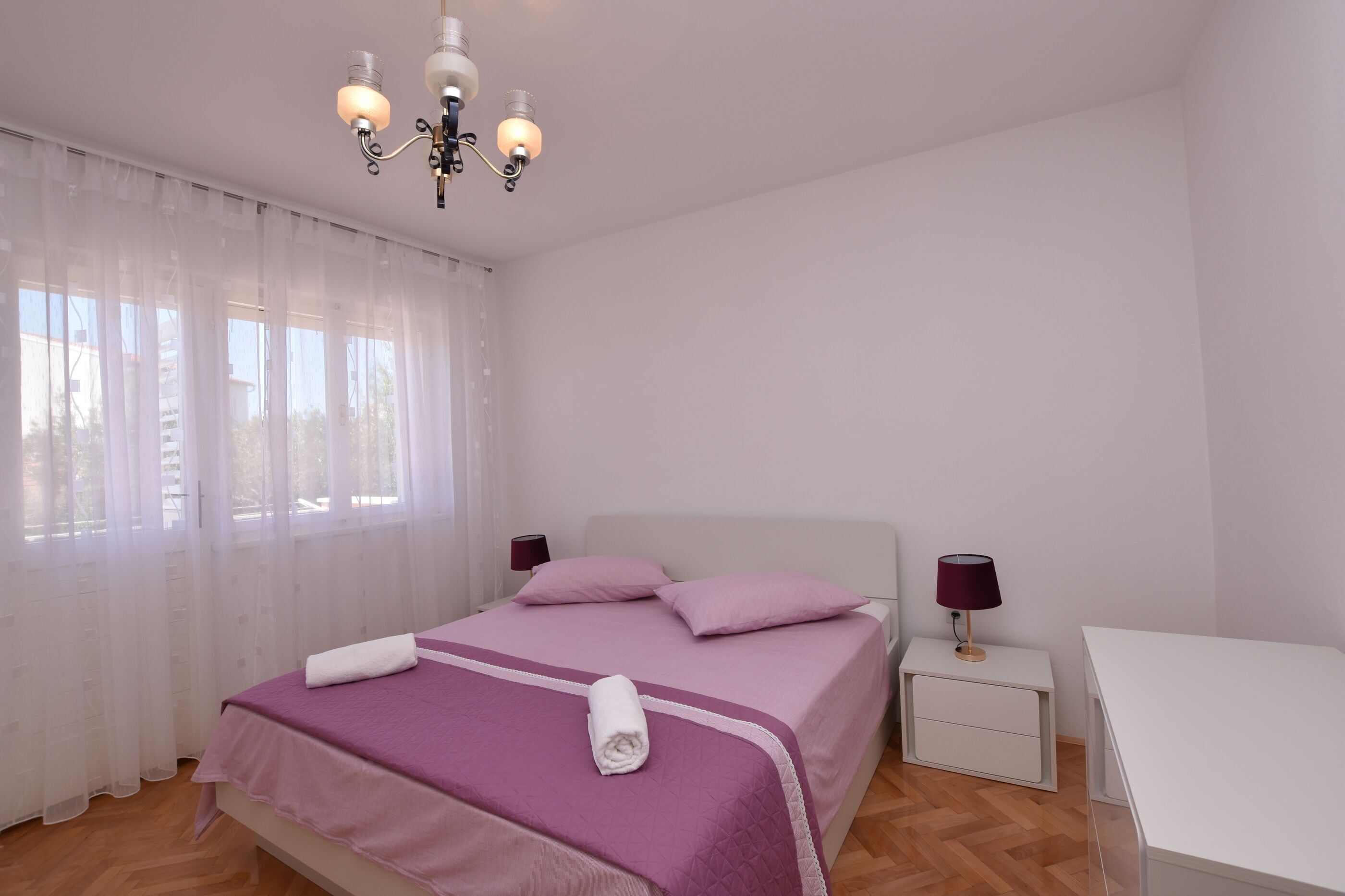 A bedroom with a bed, bedside tables, a desk, and a chandelier.