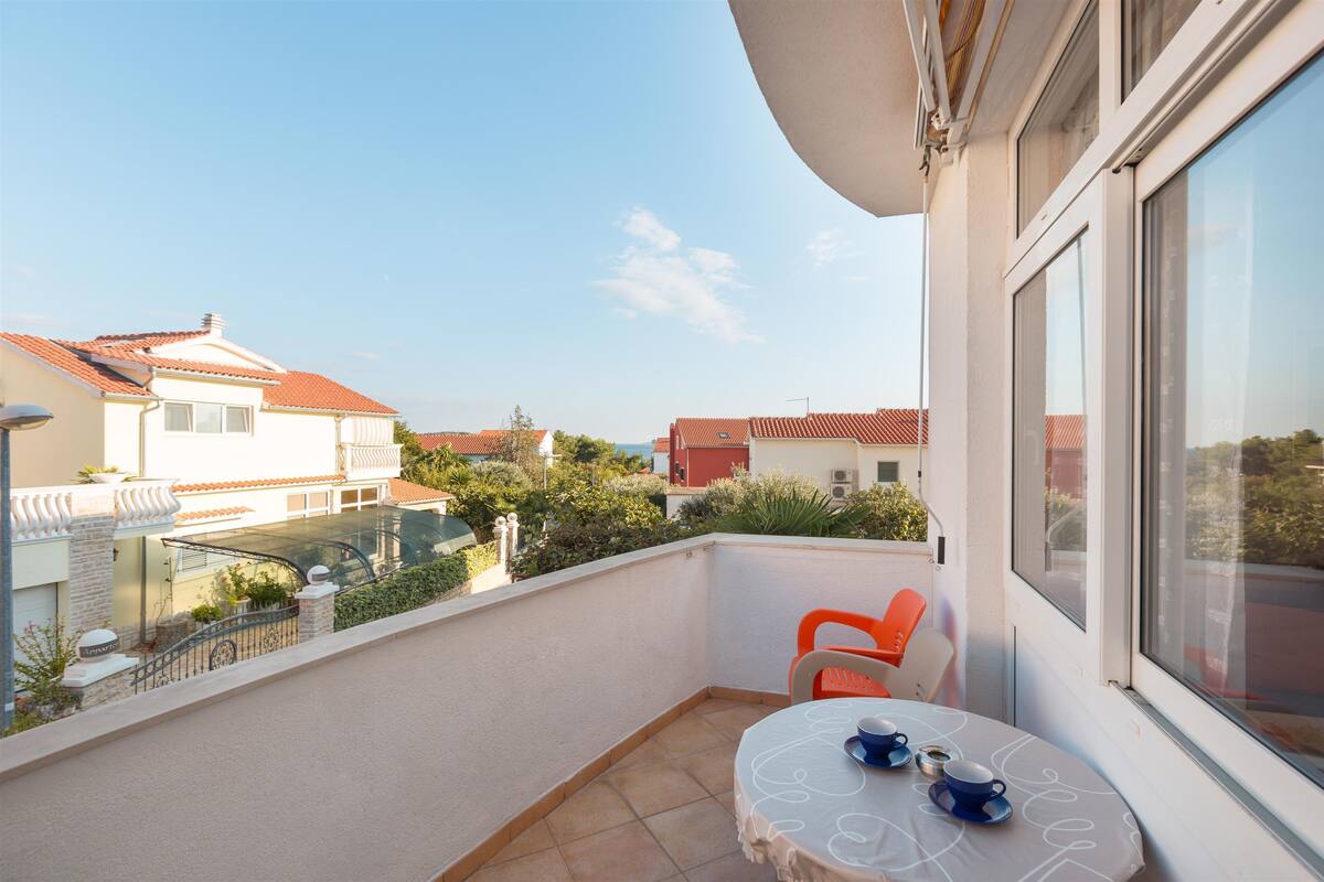 A balcony with a table and chairs, a view of neighboring houses, and a clear sky.
