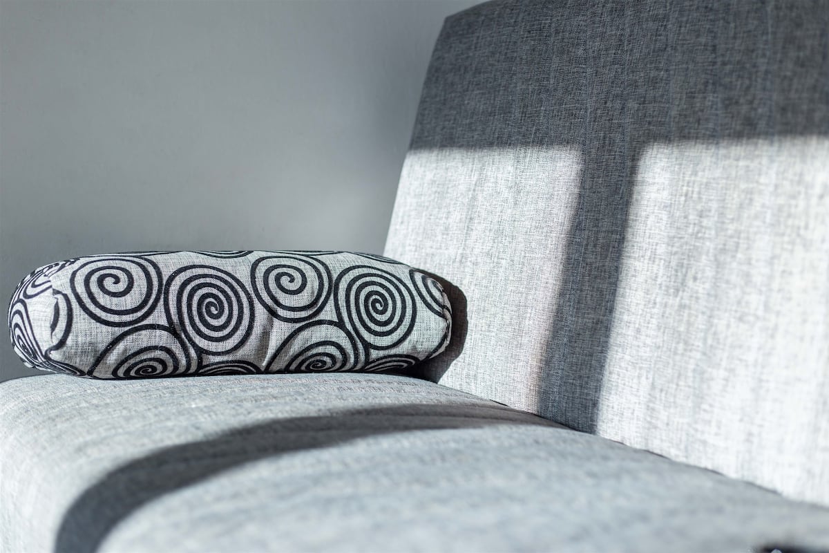 A grey upholstered chair with a patterned pillow.