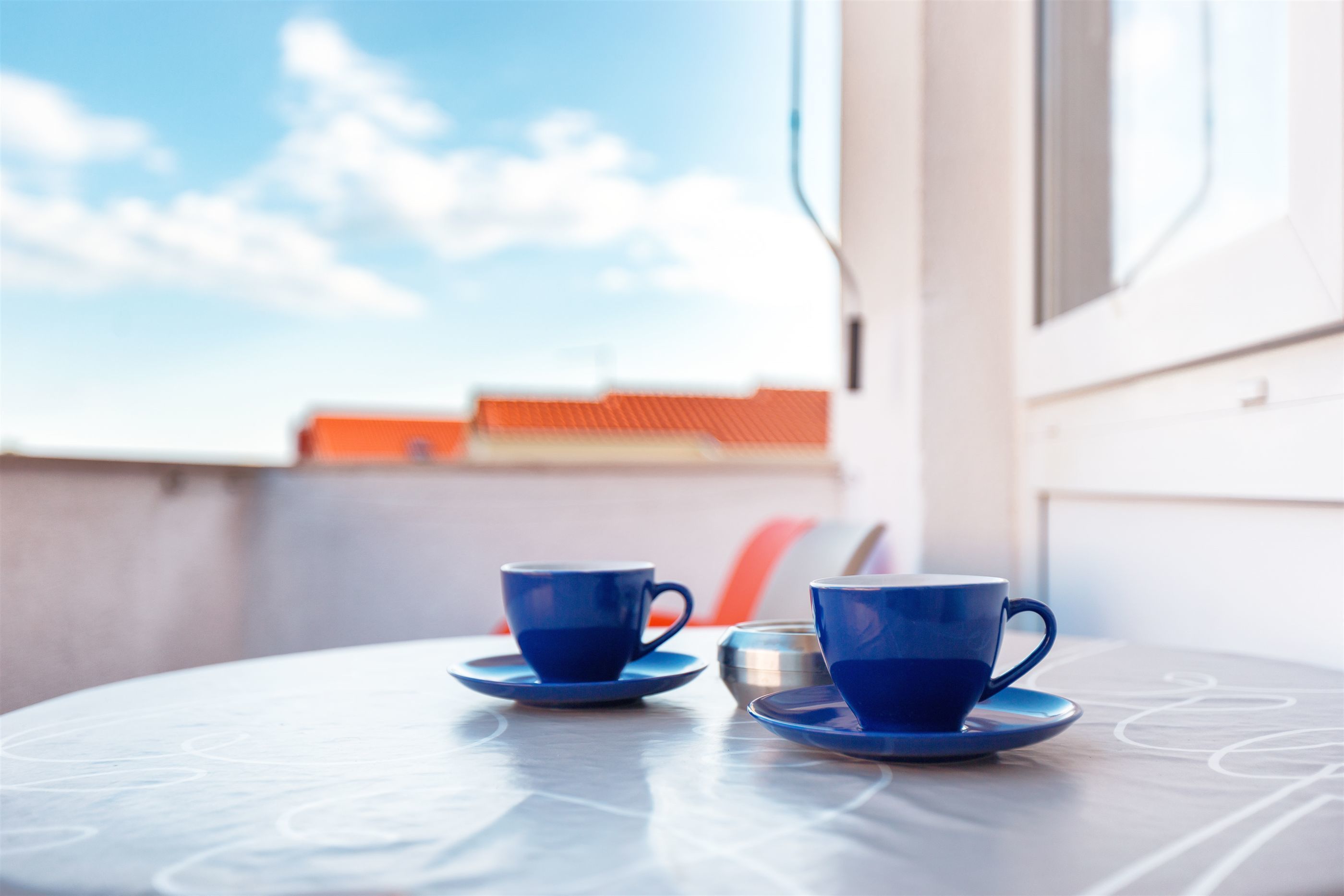Una mesa con dos tazas y platillos azules, una ventana y una vista parcial de una silla.