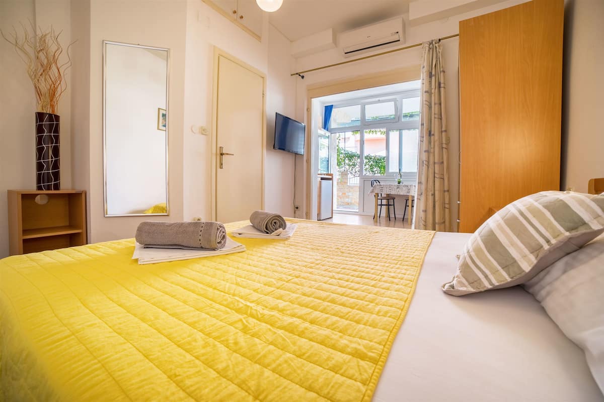 A hotel room with a large bed, a flat-screen TV, a wooden door, and a view of the outside.