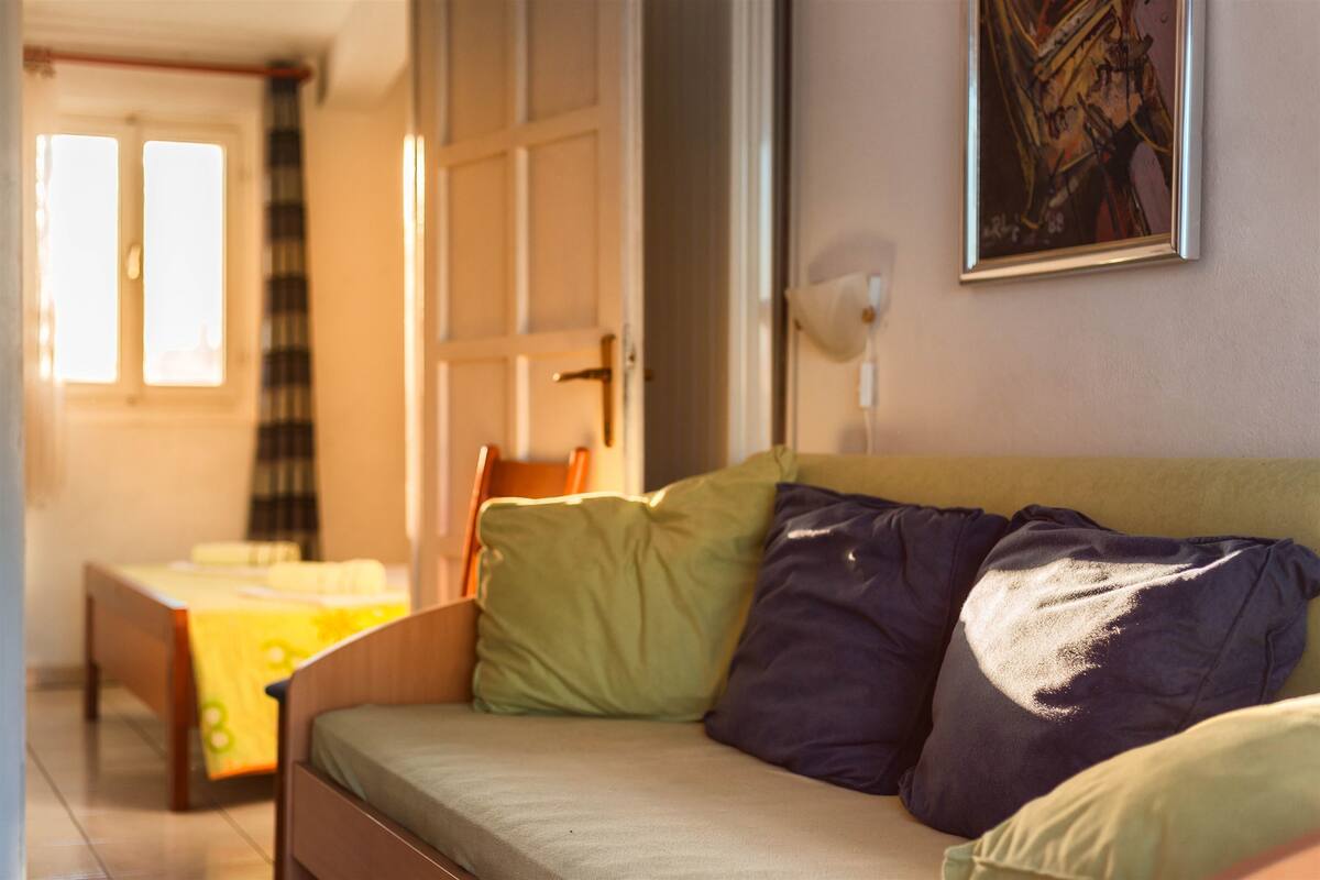A room with a bed, a sofa, a painting on the wall, and a window.