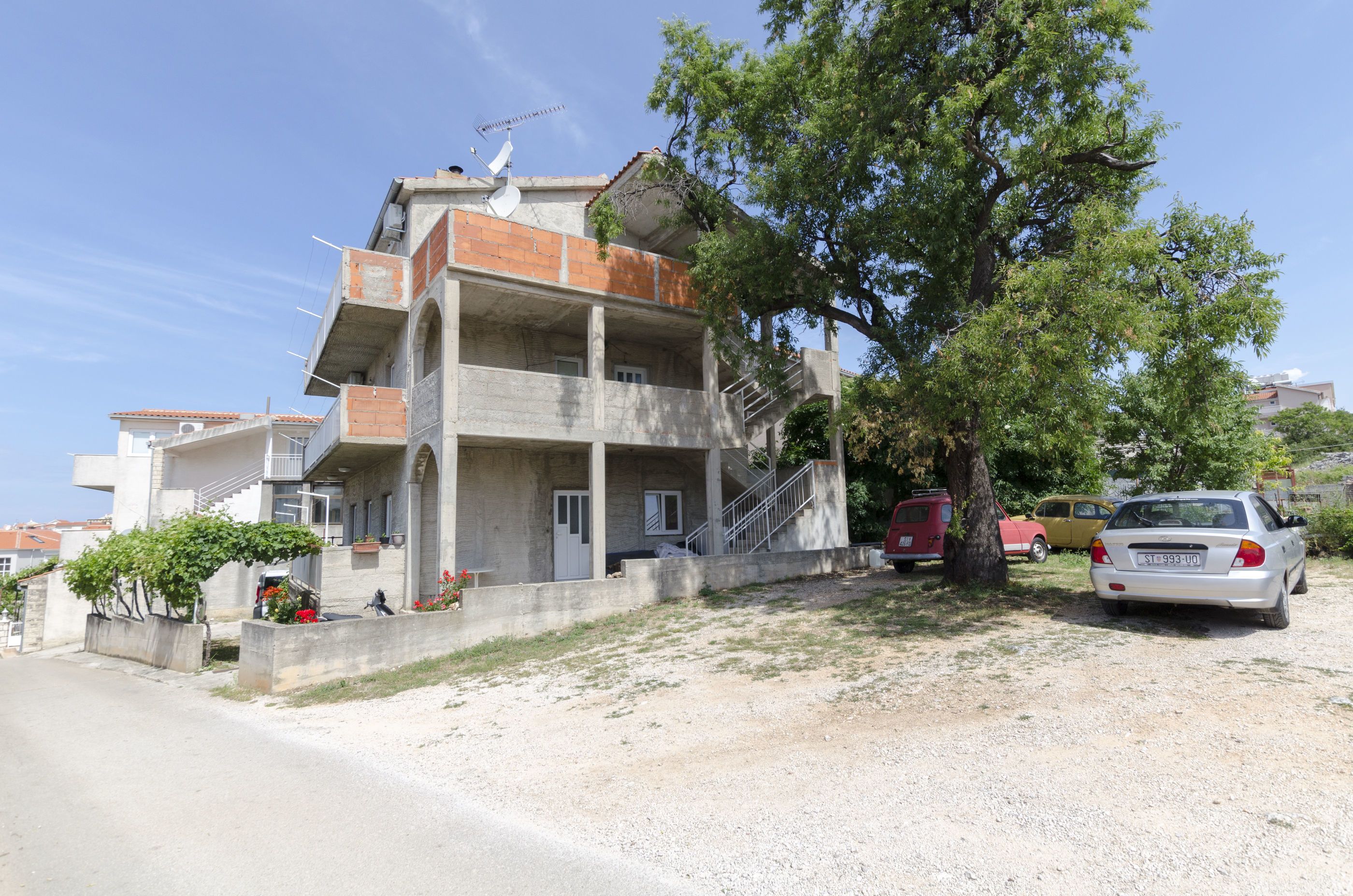 Un immeuble à plusieurs étages, doté d’une façade en béton, d’un escalier menant à l’étage supérieur et d’une voiture garée devant.