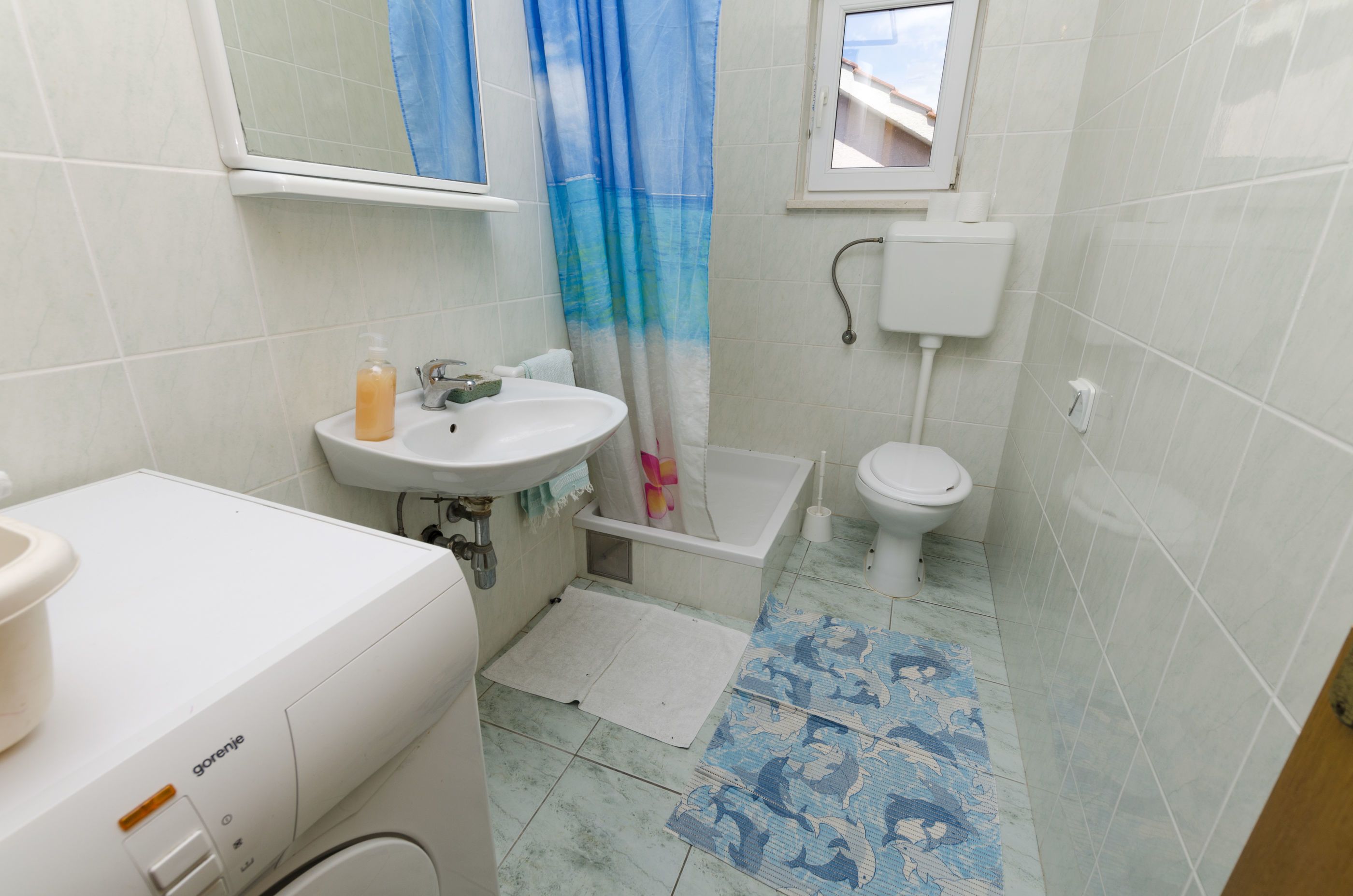Ein Badezimmer mit Waschbecken, Toilette und Badewanne. Über der Toilette befindet sich ein Fenster, und ein Duschvorhang ist sichtbar.