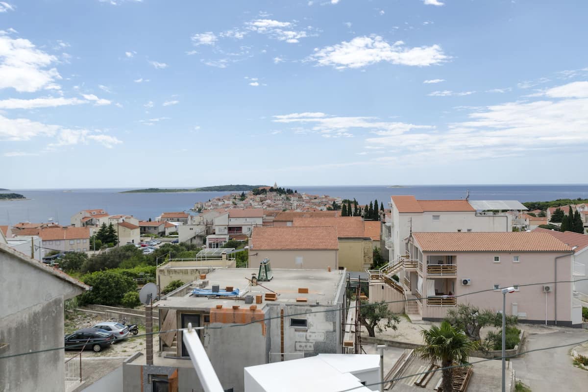 A coastal town with terracotta-roofed buildings, a clear sky, and a view of the sea.