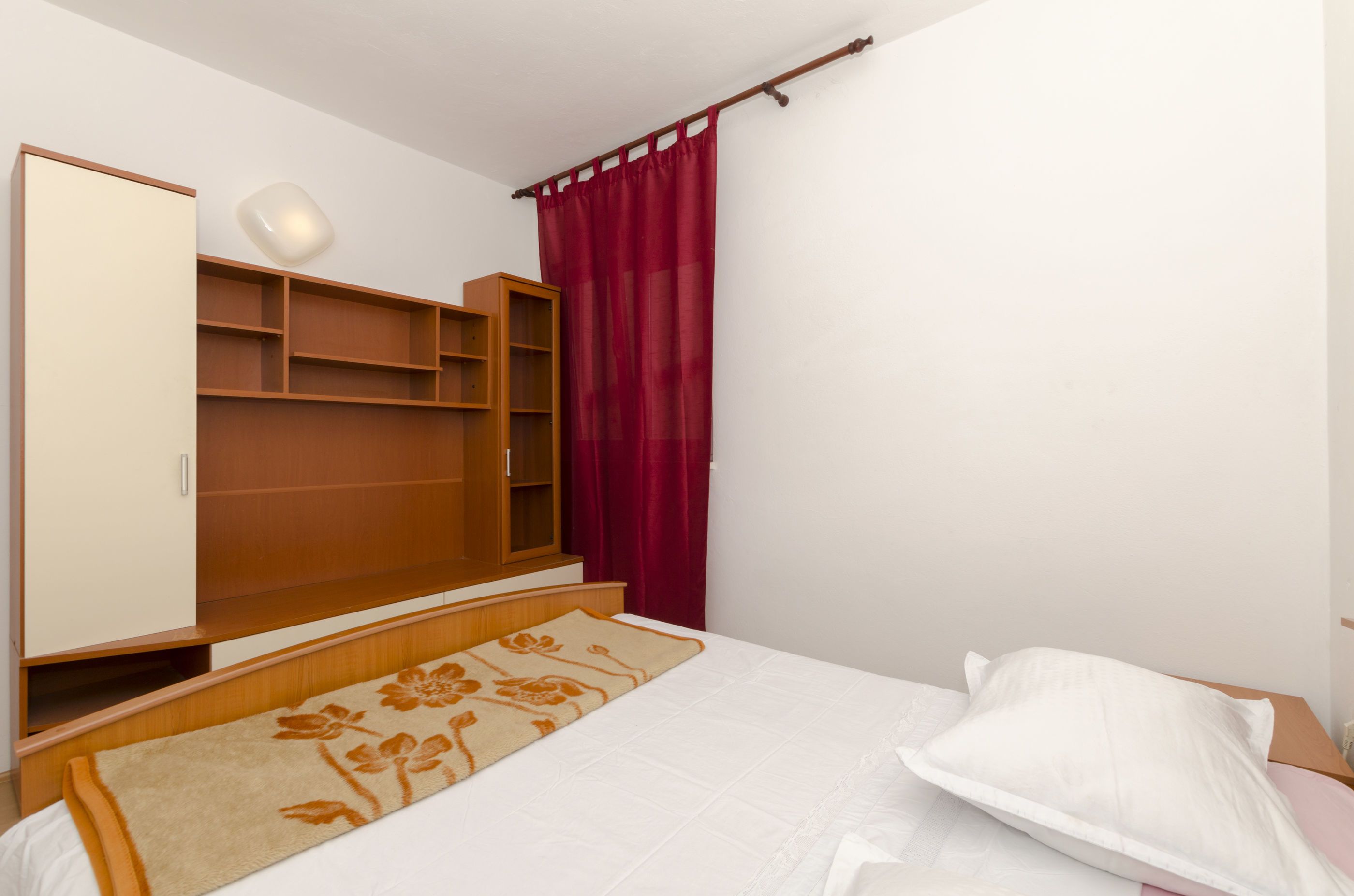 Ein Schlafzimmer mit einem Bett, einem Holzschrank, einer Regaleinheit und einem roten Vorhang.