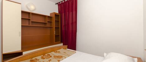 Ein Schlafzimmer mit einem Bett, einem Holzschrank, einer Regaleinheit und einem roten Vorhang.