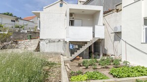 Une maison moderne à deux étages, dotée d’un balcon, d’un petit jardin et d’un mur en pierre.