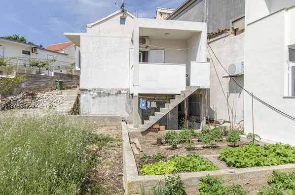 Ein modernes, zweistöckiges Haus mit Balkon, kleinem Garten und einer Steinmauer.