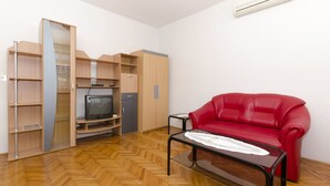 A compact living space with a red sofa, a glass-top coffee table, a television, and built-in wooden shelving. - Apartment Tome G (Primosten)