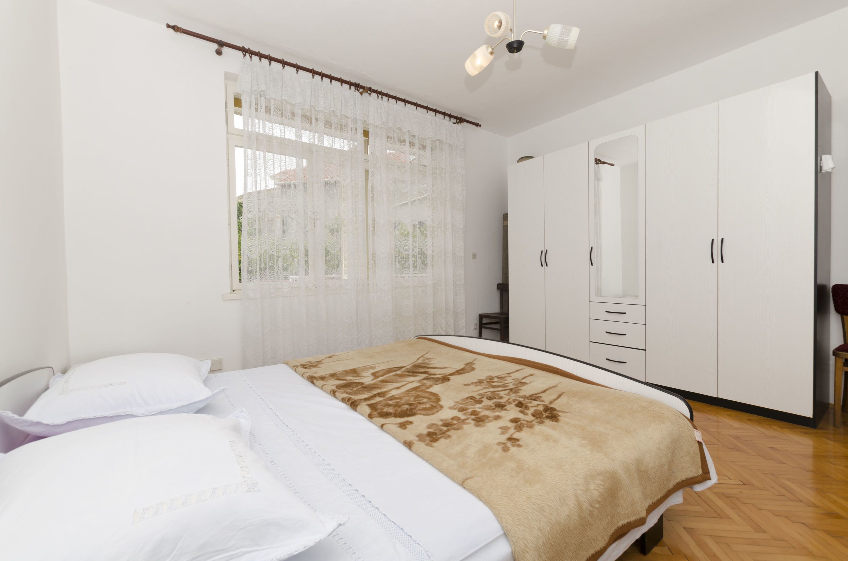 A bedroom with a bed, white curtains, a ceiling fan, and a wardrobe.