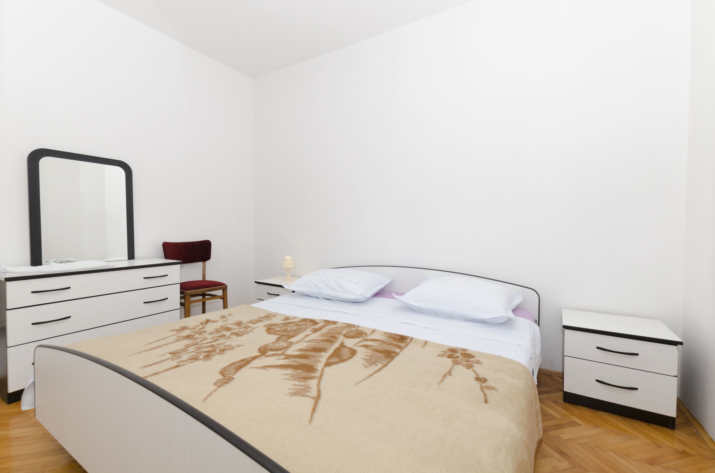 A bedroom with a bed, a dresser, a nightstand, a chair, and a mirror.