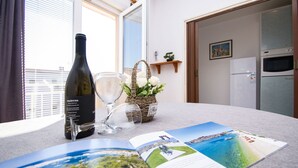 A room with a table featuring a wine bottle, a glass, and a basket with flowers. - Apartment Brko (Primosten)