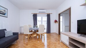 A modern living room with a sofa, dining table, chairs, a TV, and a radiator. - Apartment Brko (Primosten)