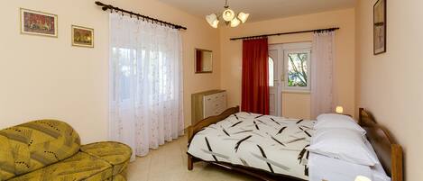 A bedroom with a bed, a chair, a nightstand, a ceiling light, and curtains.