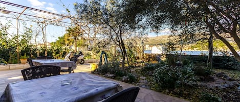 Un patio al aire libre con mesas y sillas, rodeado de follaje y vistas al mar.