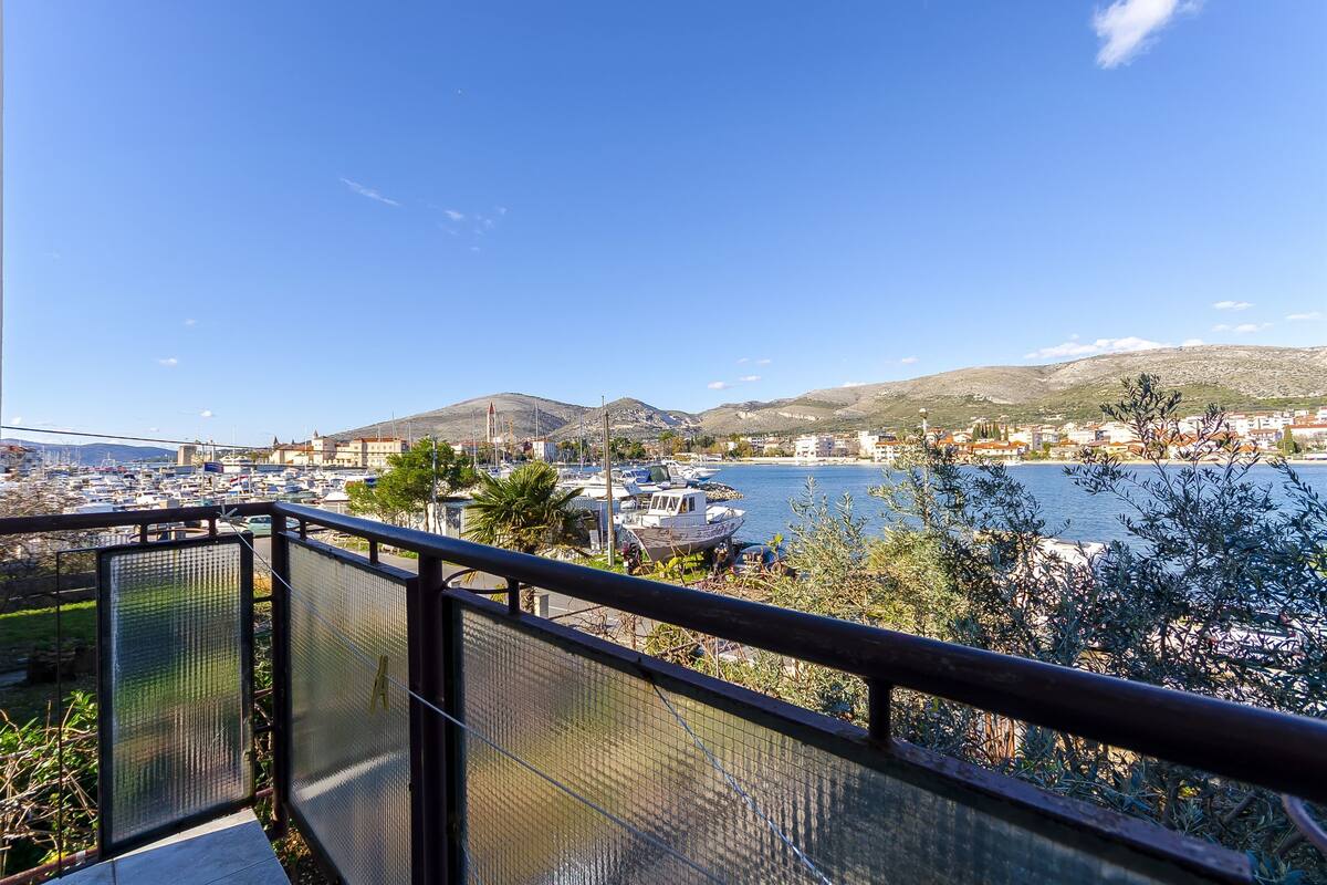 A balcony with a view of a marina, boats, and a cityscape with mountains in the background.