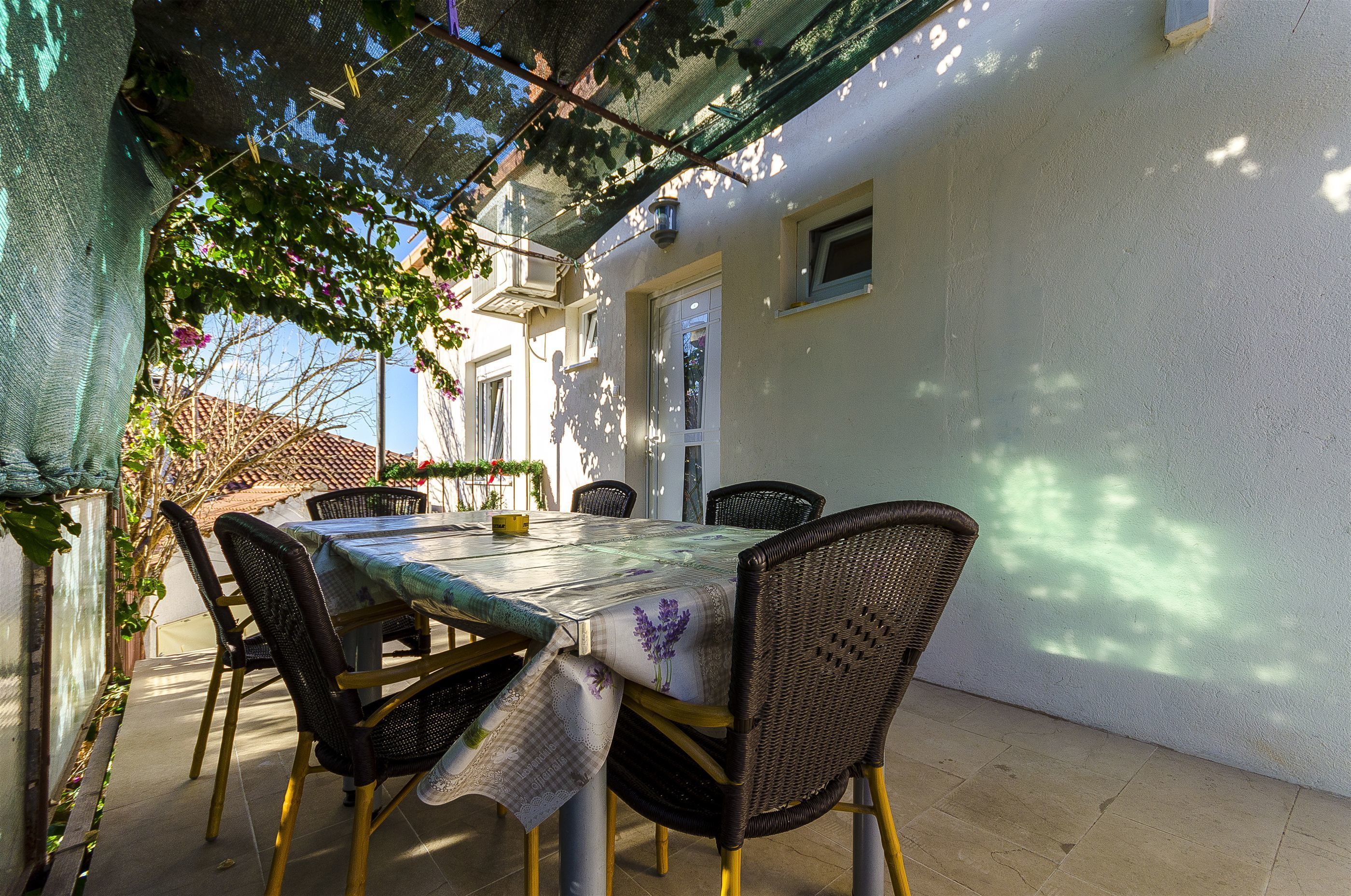 Un patio al aire libre con una mesa, sillas, una pérgola y un muro blanco.