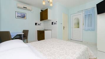 Una habitación de hotel compacta con cama, kitchenette pequeña, zona de comedor y baño.