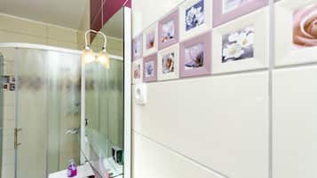 A bathroom with a glass shower enclosure, a white sink with a pink countertop, and a wall decorated with framed floral photographs.