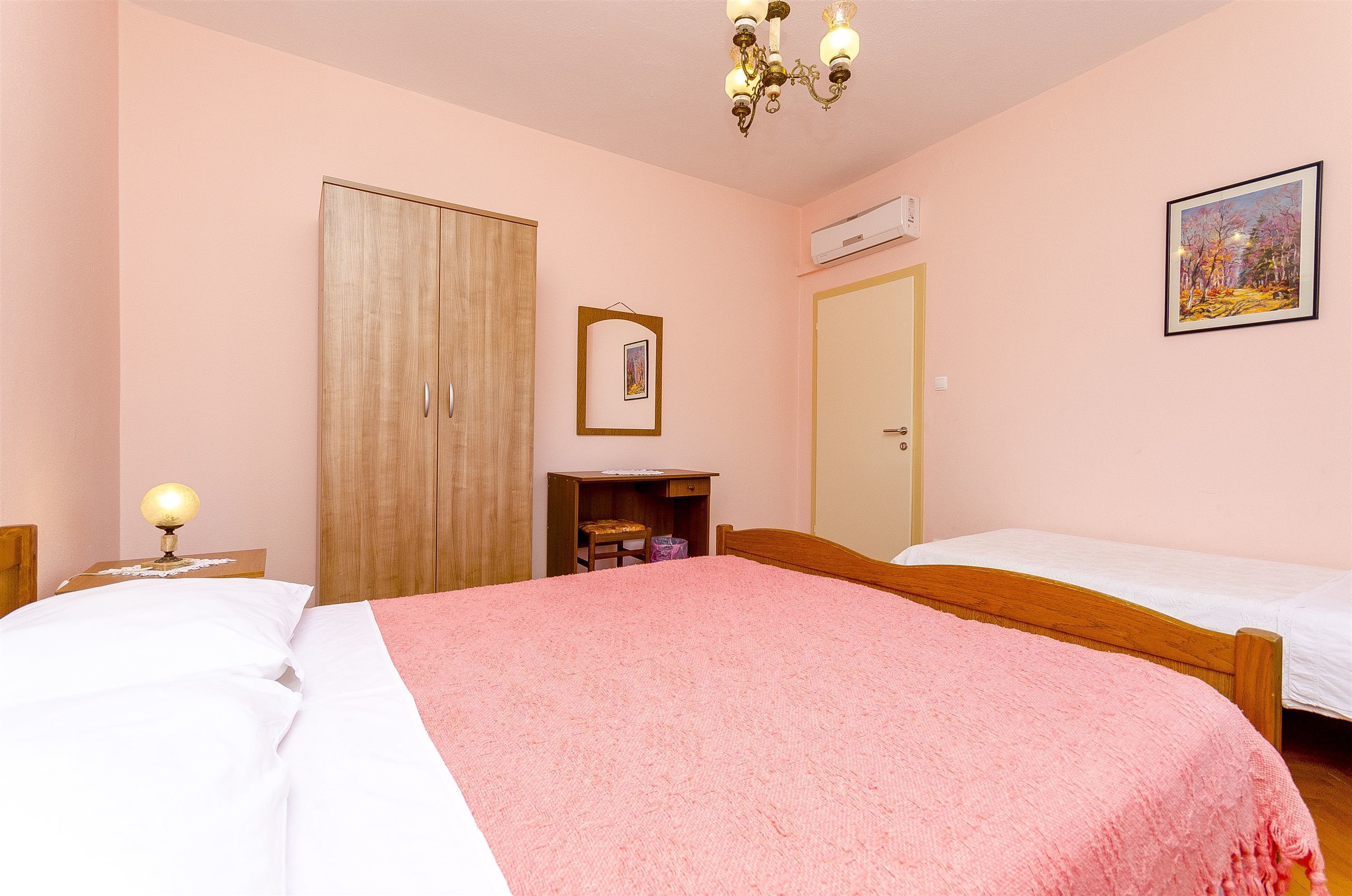 A bedroom with two beds, a wardrobe, a desk, a chair, and a painting on the wall.