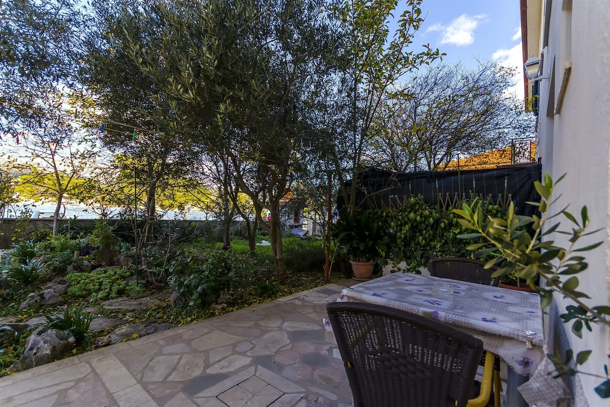 A patio area with a table and chairs, surrounded by potted plants and a stone pathway.