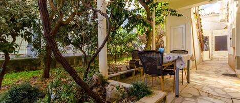 An outdoor patio area with a stone floor, a table with chairs, and a pergola with vines.