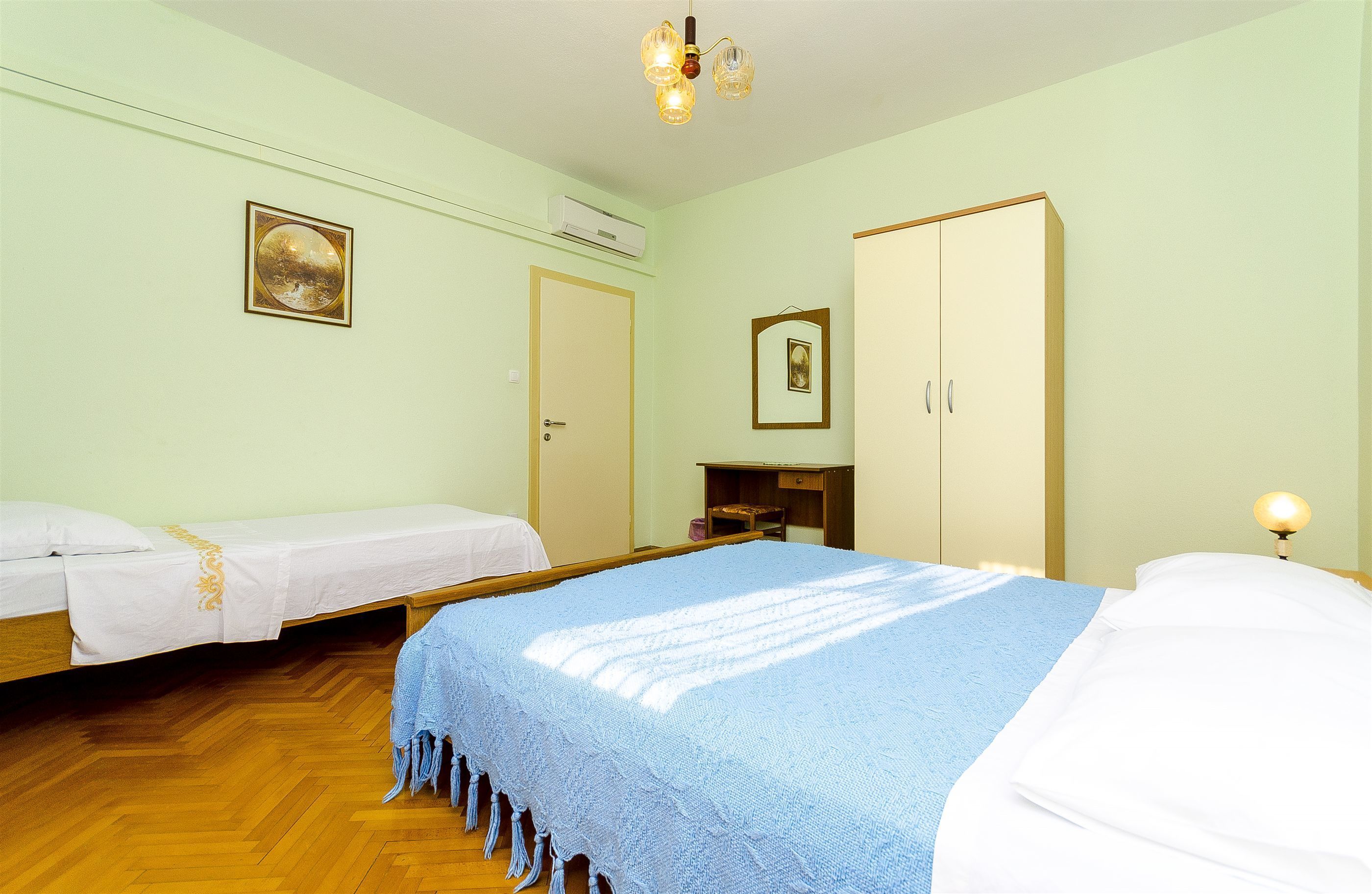 A room with two beds, a wardrobe, a desk, and a hanging light fixture.