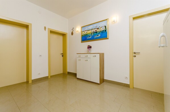 A hallway with two doors, a white cabinet with a painting above it, and a tiled floor. - Apartments Vinko (Trogir)