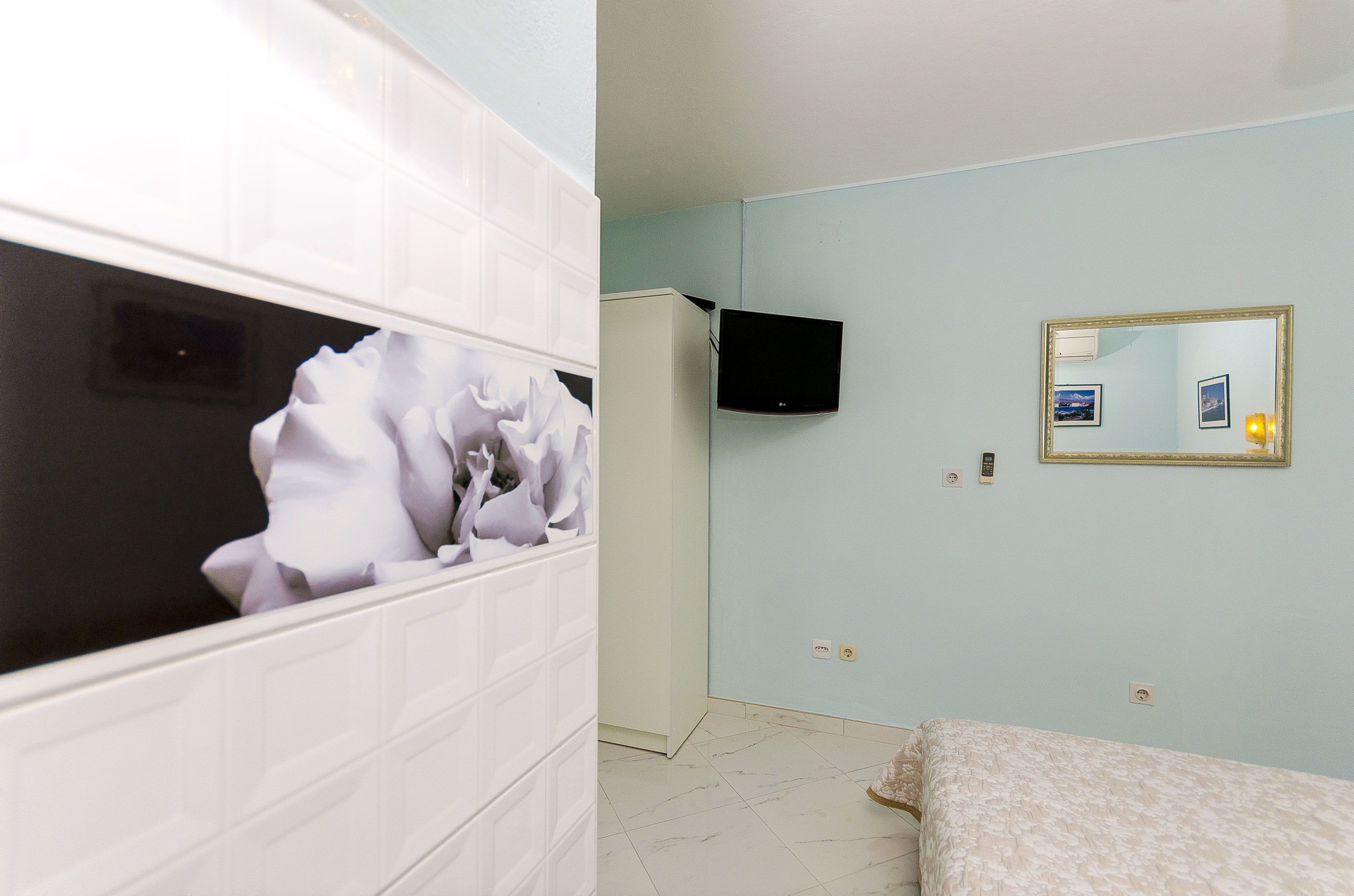 A room with a bed, a white wardrobe, a television, and a mirror on the wall.