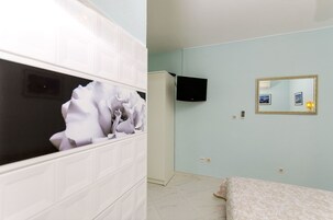 A room with a bed, a white wardrobe, a television, and a mirror on the wall.