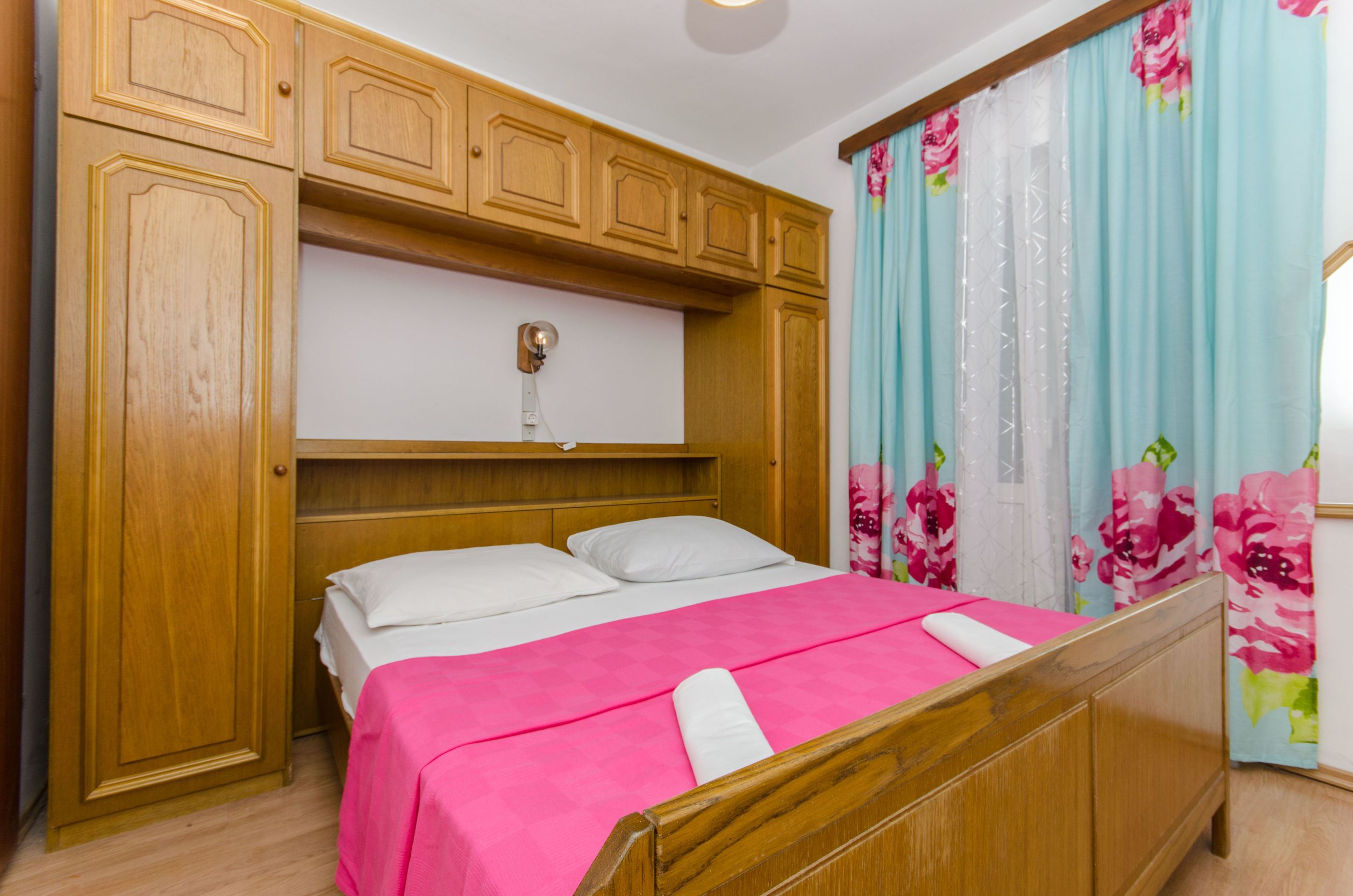 Una camera da letto con un letto di legno, una testiera bianca e una coperta rosa.