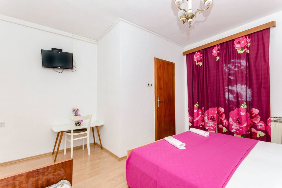 Ein Schlafzimmer mit Bett, Schreibtisch, Stuhl, Fernseher und einer Tür.