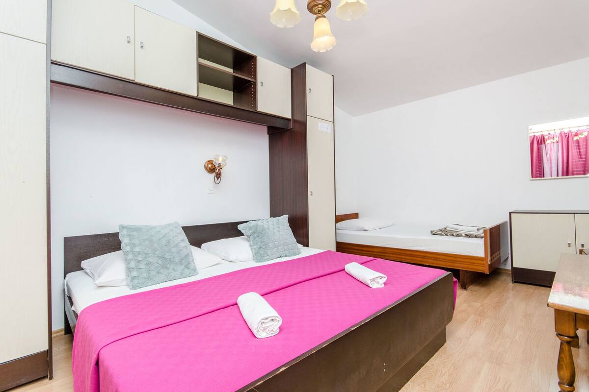 Ein Hotelzimmer mit einem großen Bett, einem kleineren Bett, einem Schreibtisch und einem Kleiderschrank.