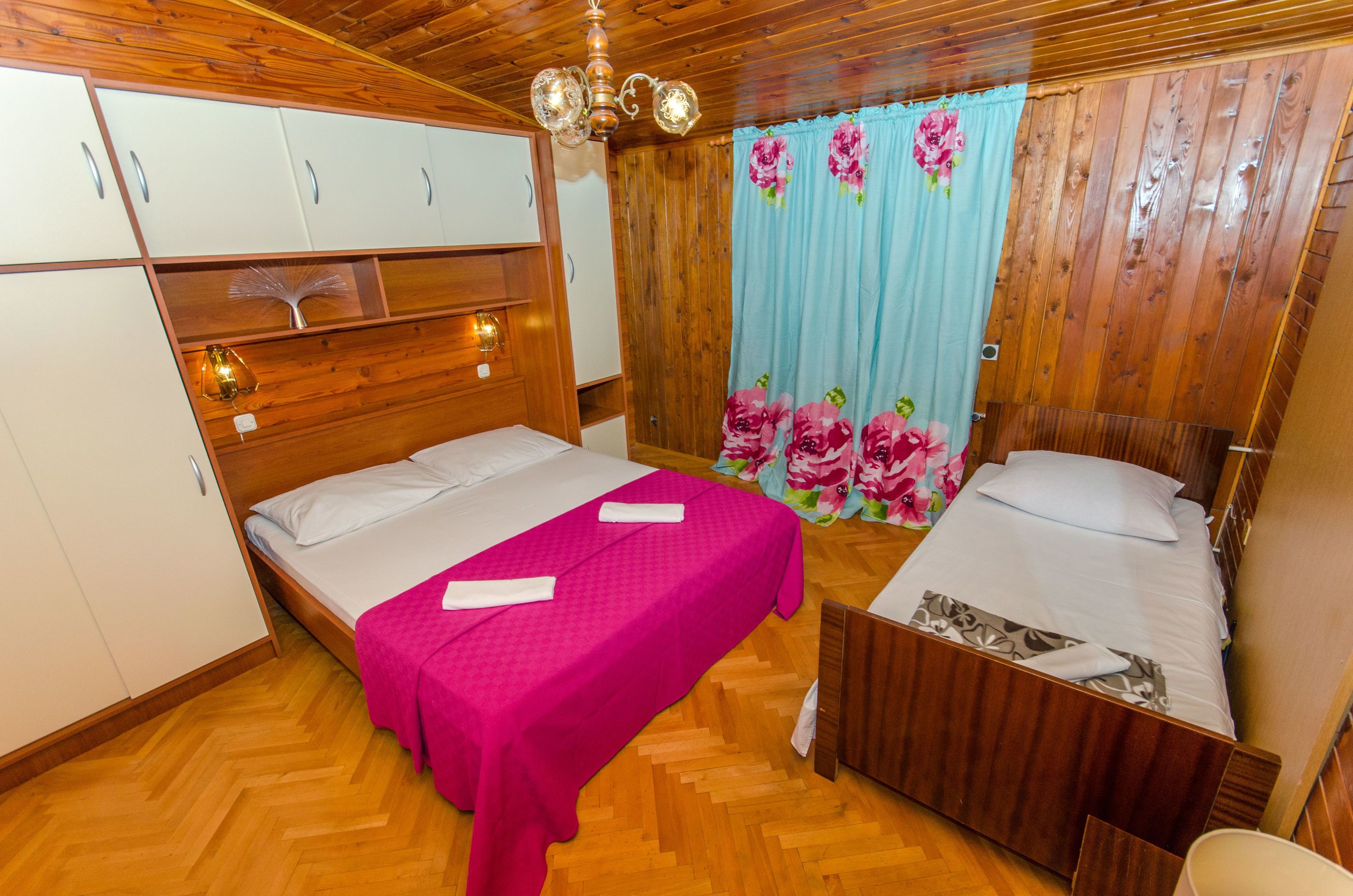Una habitación con dos camas, piso de madera, un armario y una cortina estampada.