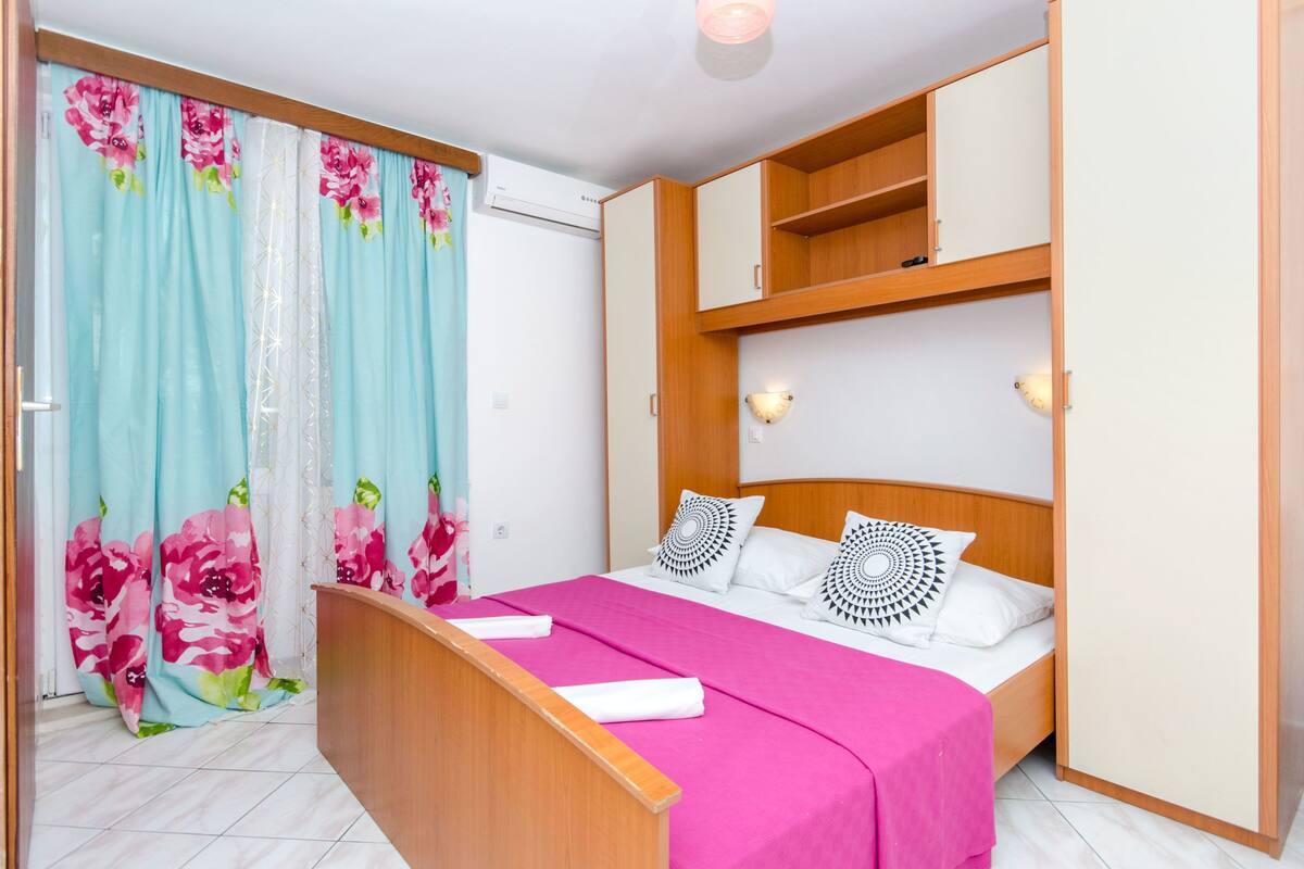 Ein Schlafzimmer mit einem Bett, einem Holzschrank, einem Schreibtisch und einem Vorhang mit Blumenmuster.